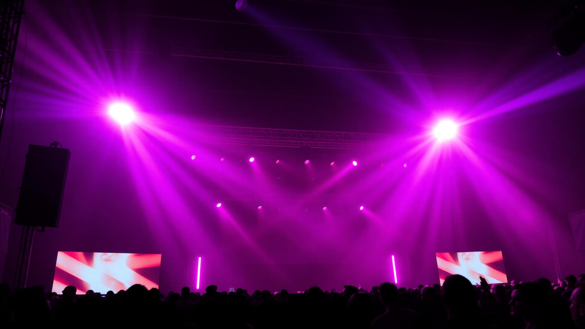 Live concert stage bathed in magenta and blue light with an LED screen